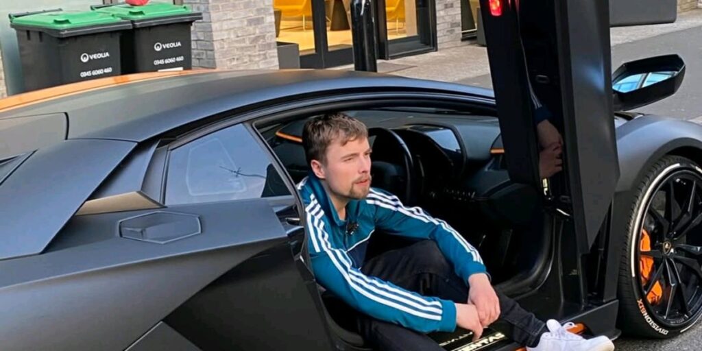 Jimmy NoCap sitting inside a luxury car wearing designer clothes and gold jewelry
